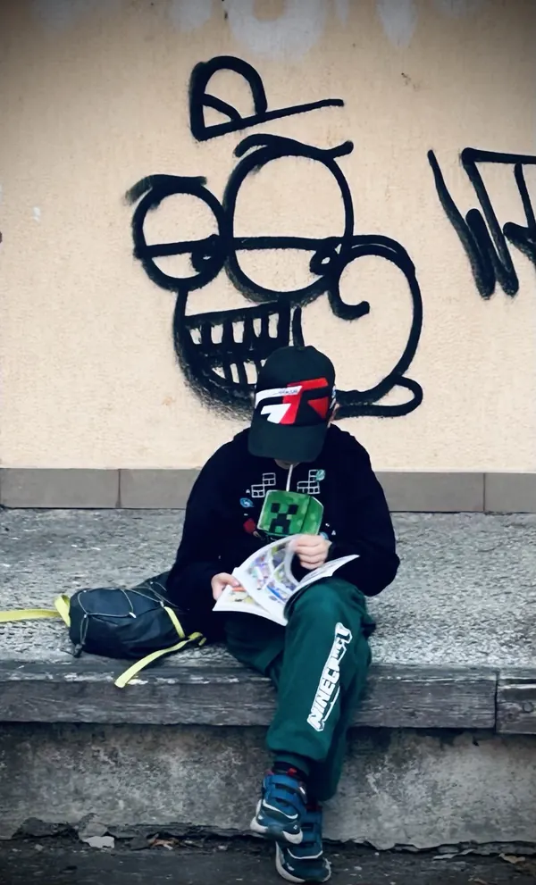 Jasiek czyta komiks pod murem z graffiti